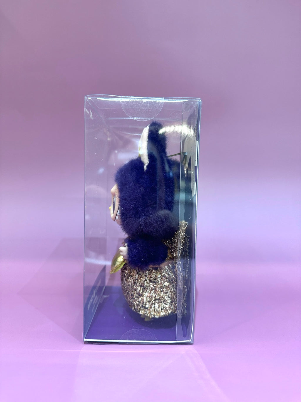 Decorative item with blue pom-poms and gold accents in a clear box on a pink background