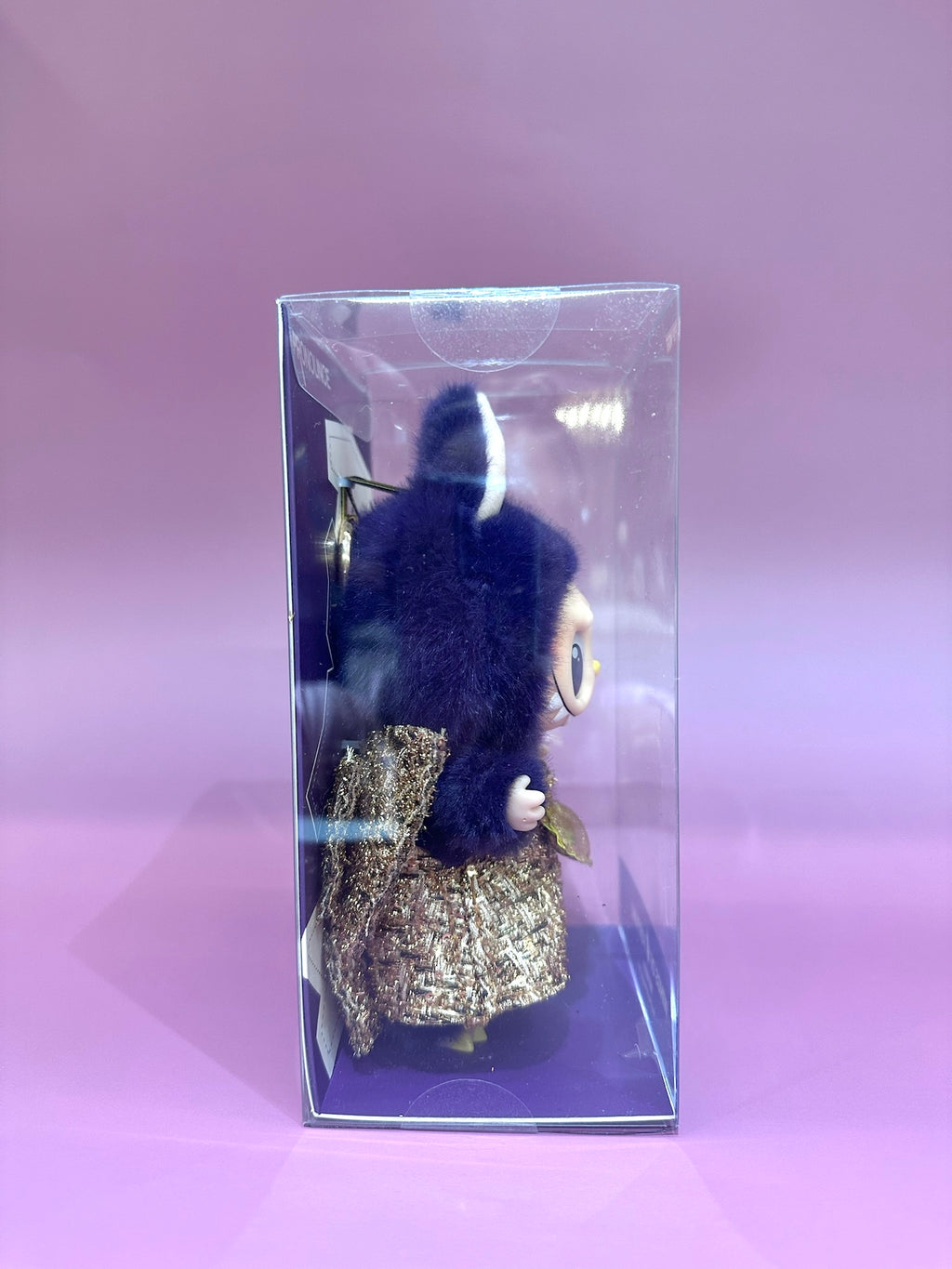 Keychain with blue fur and gold glittery design in clear packaging on a pink background