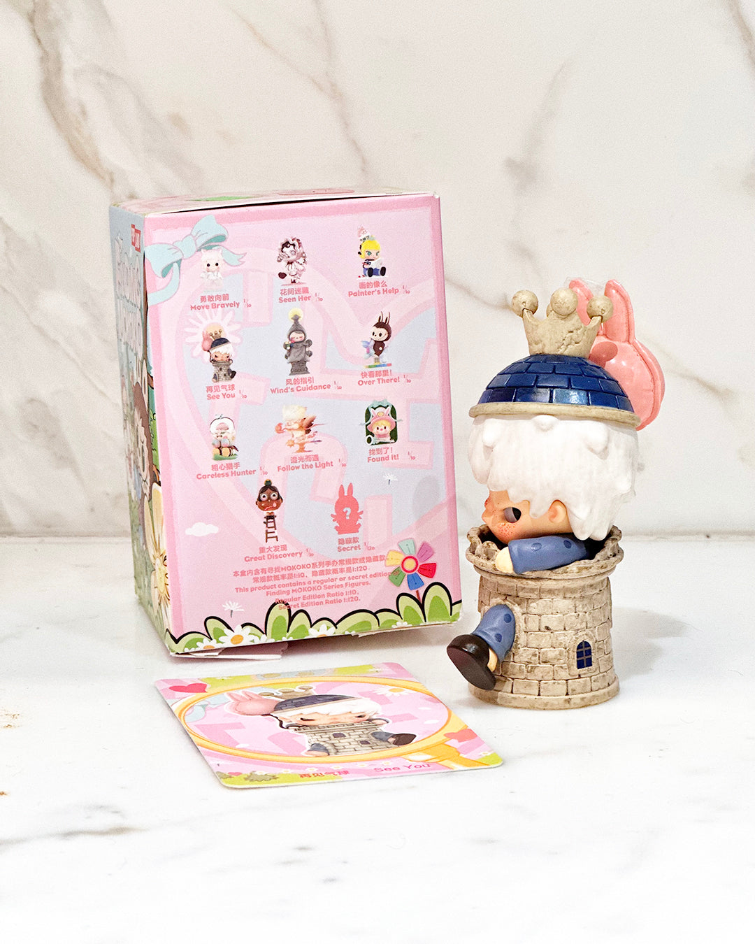 Toy figure in a small house with a pink packaging guide on a white background