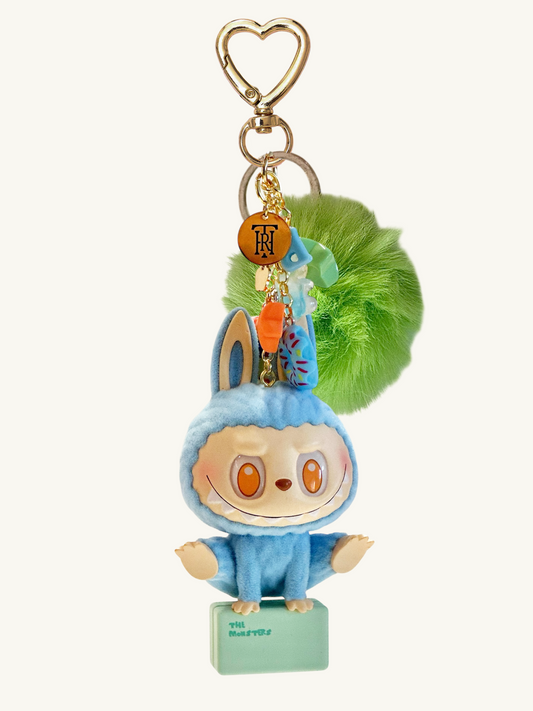 Plush keychain with a character in a blue outfit and green pom-pom on a white background