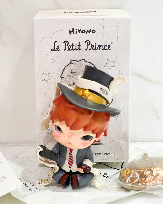 Figurine of a character from 'Le Petit Prince' with a top hat and suit, standing in front of a branded box.
