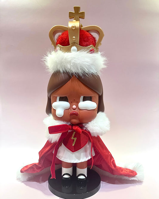 Toy figure with a crown, red cape, and white fur on a light pink background