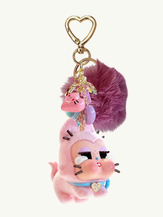 Pink cartoon character keychain with purple fluffy ball and heart-shaped keyring on a white background